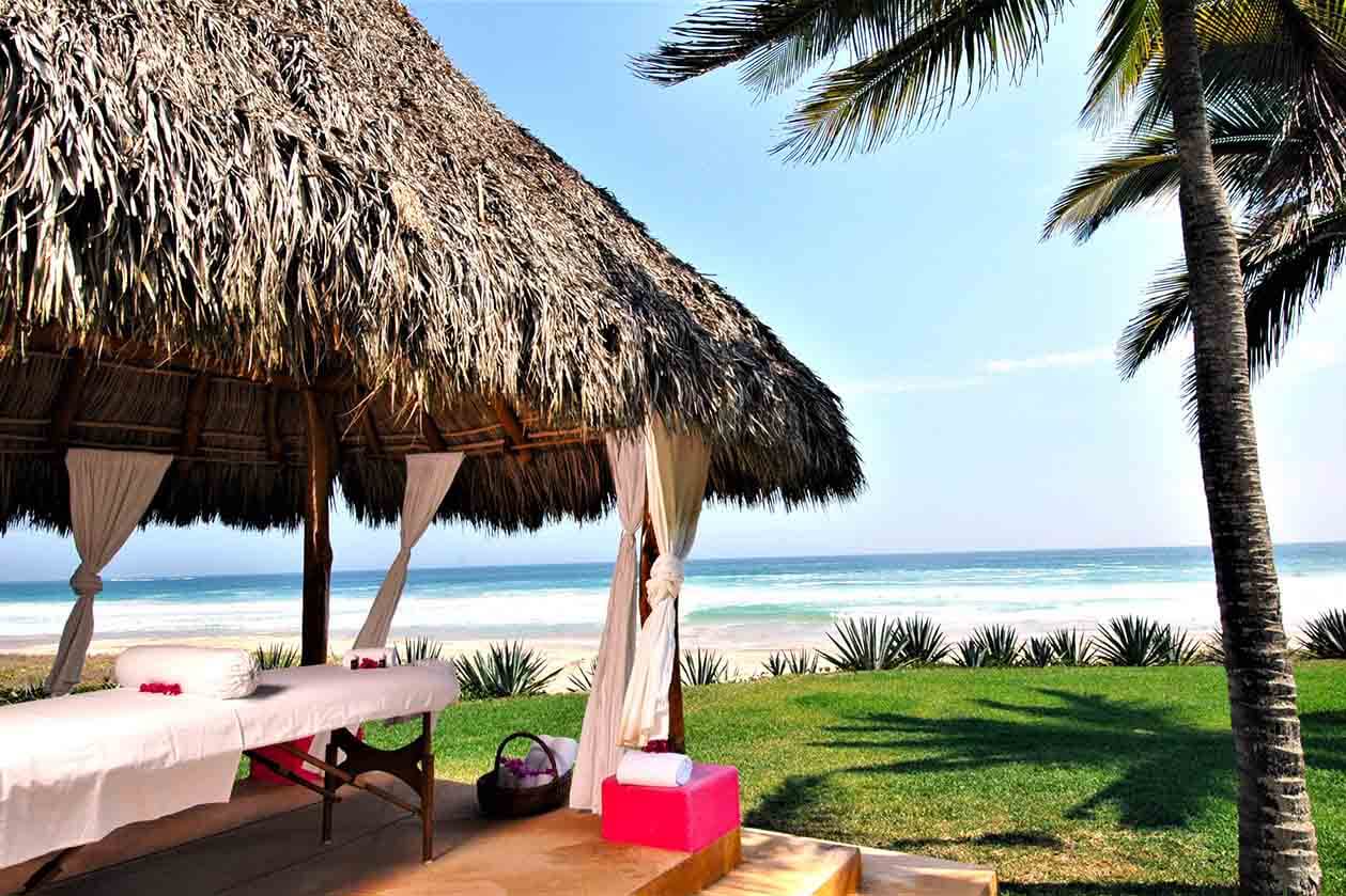 Área de masajes al aire libre bajo una palapa cerca de la playa del hotel las Alamandas